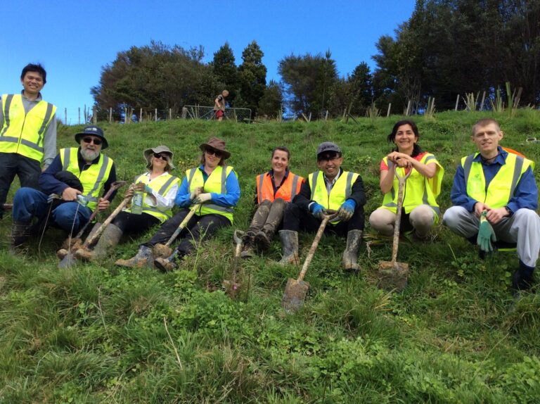 Volunteers with spades resting on a hillside after planting native trees on a New Zealand conservation project
