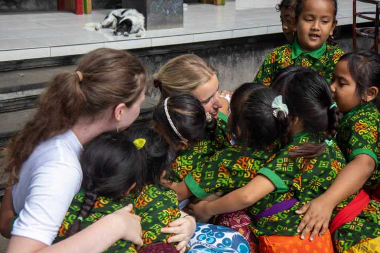 A Volunteering Solutions volunteer sitting with kindergarten children in matching green uniforms at a day centre in Bali