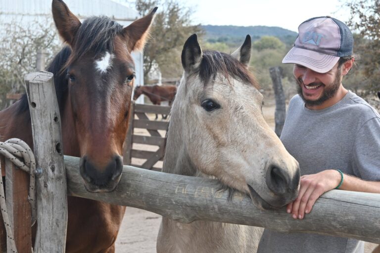 Volunteer greeting two rescued horses over a fence at the horse sanctuary in the hills of Córdoba, Argentina