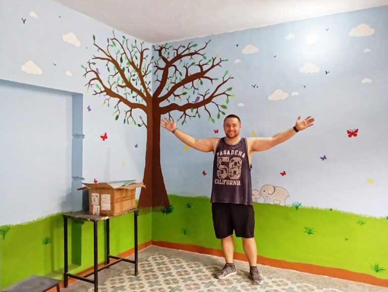 A Volunteering Solutions volunteer standing in a community centre classroom he has just repainted with a tree and butterfly mural