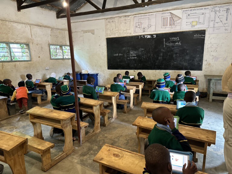 Pupils using tablets in a classroom supported by volunteers in Arusha, Tanzania