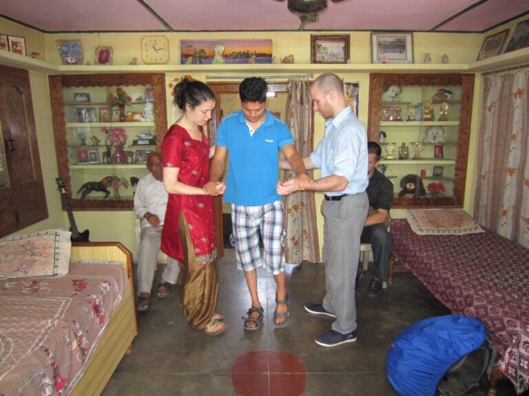 Two volunteers supporting a young man to walk during a mobility session at a special needs project