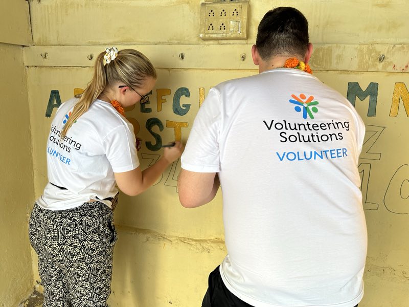 Two Volunteering Solutions volunteers painting an alphabet wall at a school